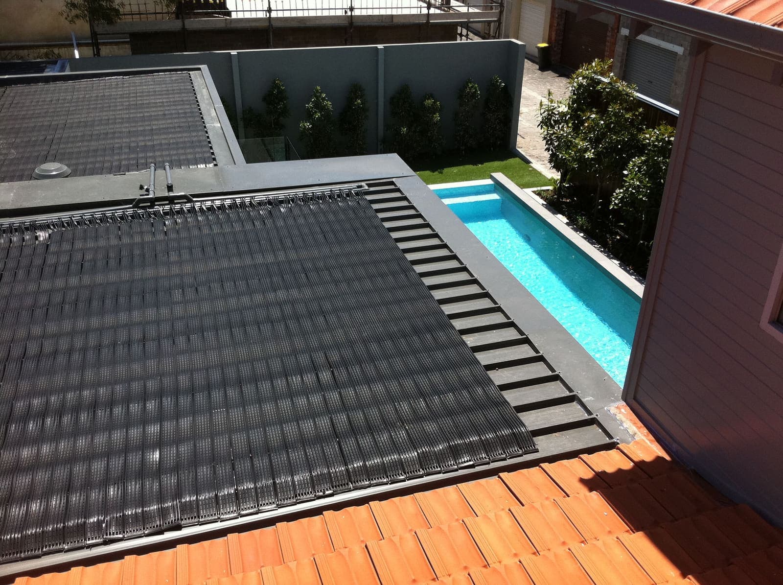 Solar pool heating panels installed on a residential roof with pool visible below
